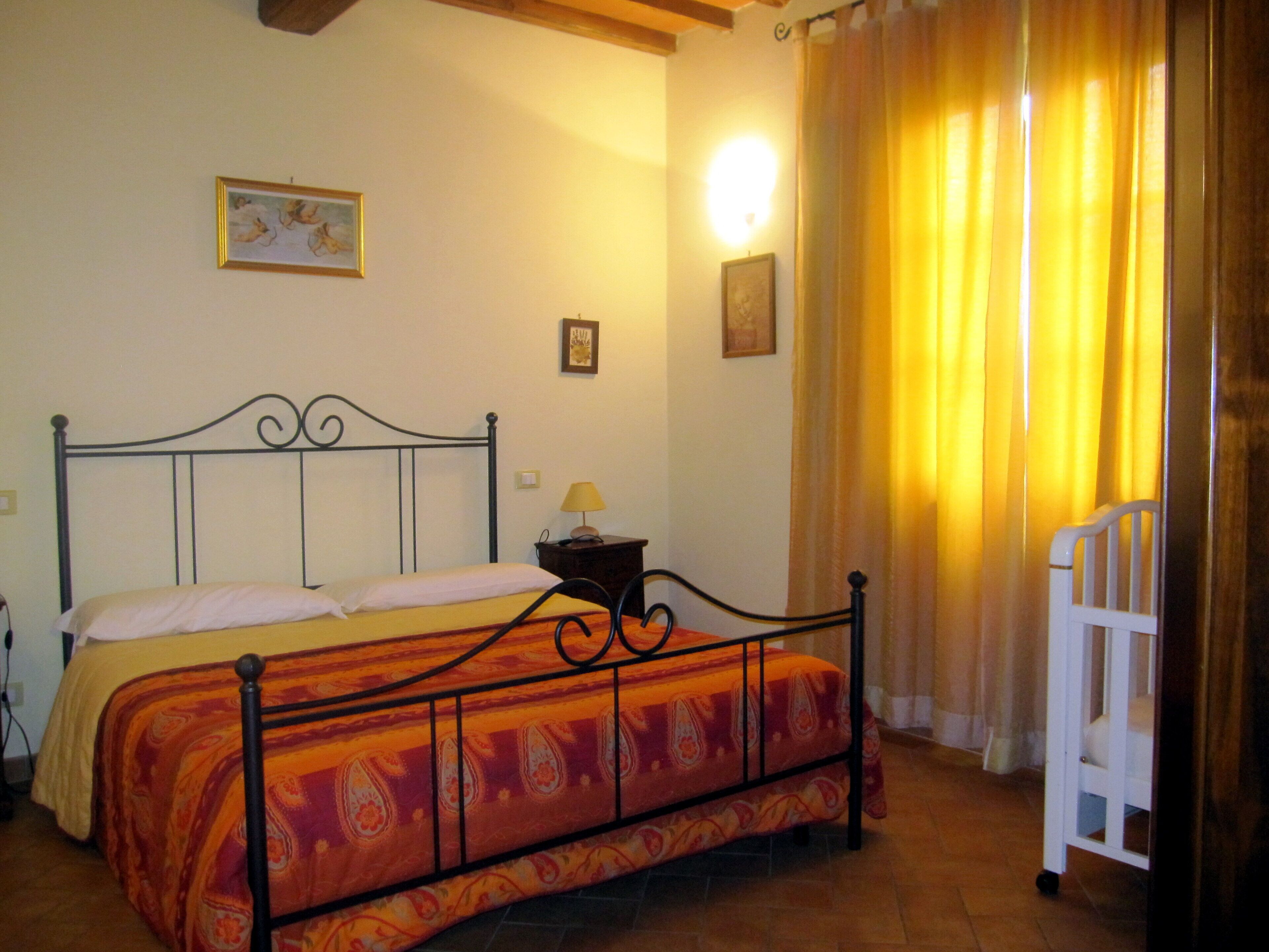 A bedroom with a bed, a nightstand, a lamp, a chair, and two framed pictures on the wall.
