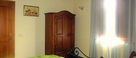 A bedroom with a bed, wooden wardrobe, and a window with curtains.