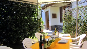 An outdoor dining area with a table set for four, surrounded by white plastic chairs. There are wine bottles, a fruit bowl, and plates on the table. - POGGIO ALLA CAVALLA FARMHOUSE with swimming pool in the heart of Tuscany (Toscana)