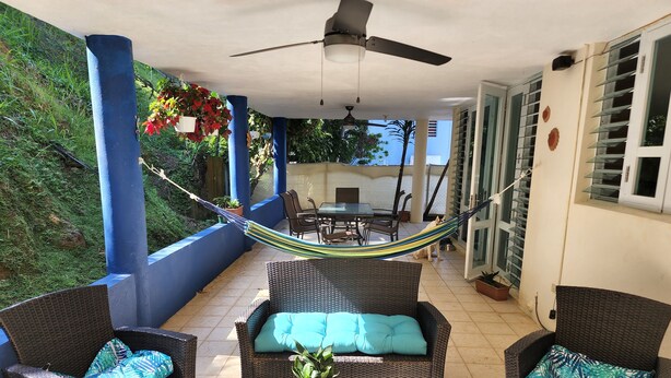 A covered patio area with wicker furniture, a hammock, and potted plants. - Cozy private room in shared residence with pool (San Juan)
