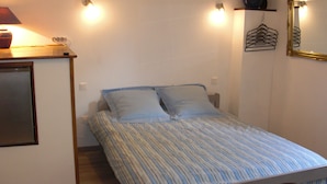 Ein kleines Zimmer mit einem Einzelbett, einer Bettdecke mit Streifen, einem Nachttisch mit Lampe und einem Spiegel an der Wand.