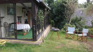 Eine überdachte Terrasse mit Tisch und Stühlen, ein Gartenschlauch und eine Gartenanlage mit Sitzgelegenheiten und einem kleinen Tisch.