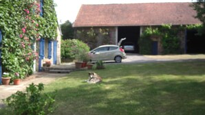 Ein Haus mit rotem Dach, einer Garage und einem davor geparkten Auto. Ein Hund liegt auf der Wiese vor dem Haus.
