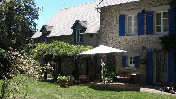 Ein Steinhaus mit geneigtem Dach, ein Garten mit Kübelpflanzen und eine Bank.