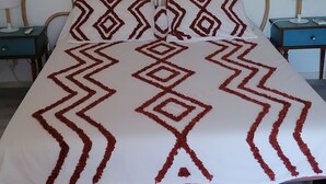 A bed with a geometric patterned bedspread, a round headboard, and a wall-mounted decorative item above it.