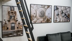 Tres cuadros enmarcados en una pared, una escalera negra apoyada contra la pared y un sofá de color oscuro.