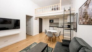 Un apartamento moderno con habitación tipo loft, comedor y sala de estar con televisor grande y sofá.