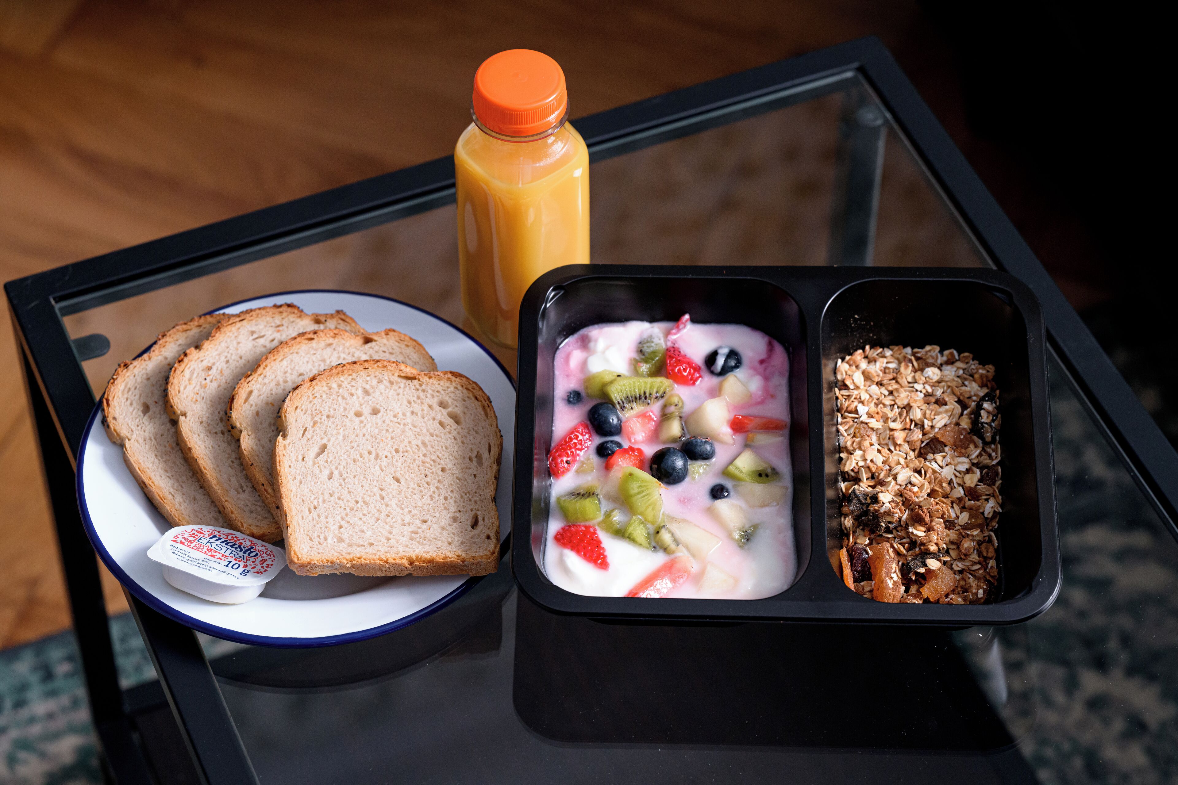 A breakfast tray with toast, yogurt with fruits, and granola on a glass table.