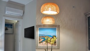 Un comedor con una mesa, sillas, una orquídea en maceta, un televisor montado en la pared y un ventanal con vistas al paisaje costero.