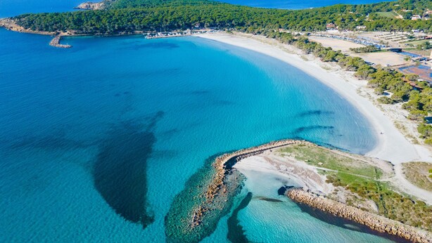 Vista aérea de una zona costera con mar azul cristalino, una playa de arena y un litoral rocoso.