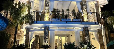 Un edificio de dos pisos con un balcón, columnas y plantas en macetas.