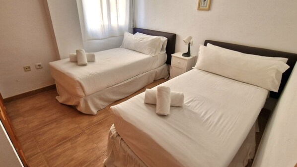 A hotel room with two beds, each with neatly folded towels and white linens. - Apartamentos Latin  (Nerja)