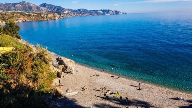 A beach with clear blue water, rocky terrain, and mountains in the background. - Apartamentos Latin  (Nerja)