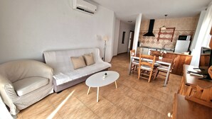 A living room with a sofa, a dining table with chairs, a small round table, and a kitchen area with a microwave and stove. - Apartamentos Latin  (Nerja)