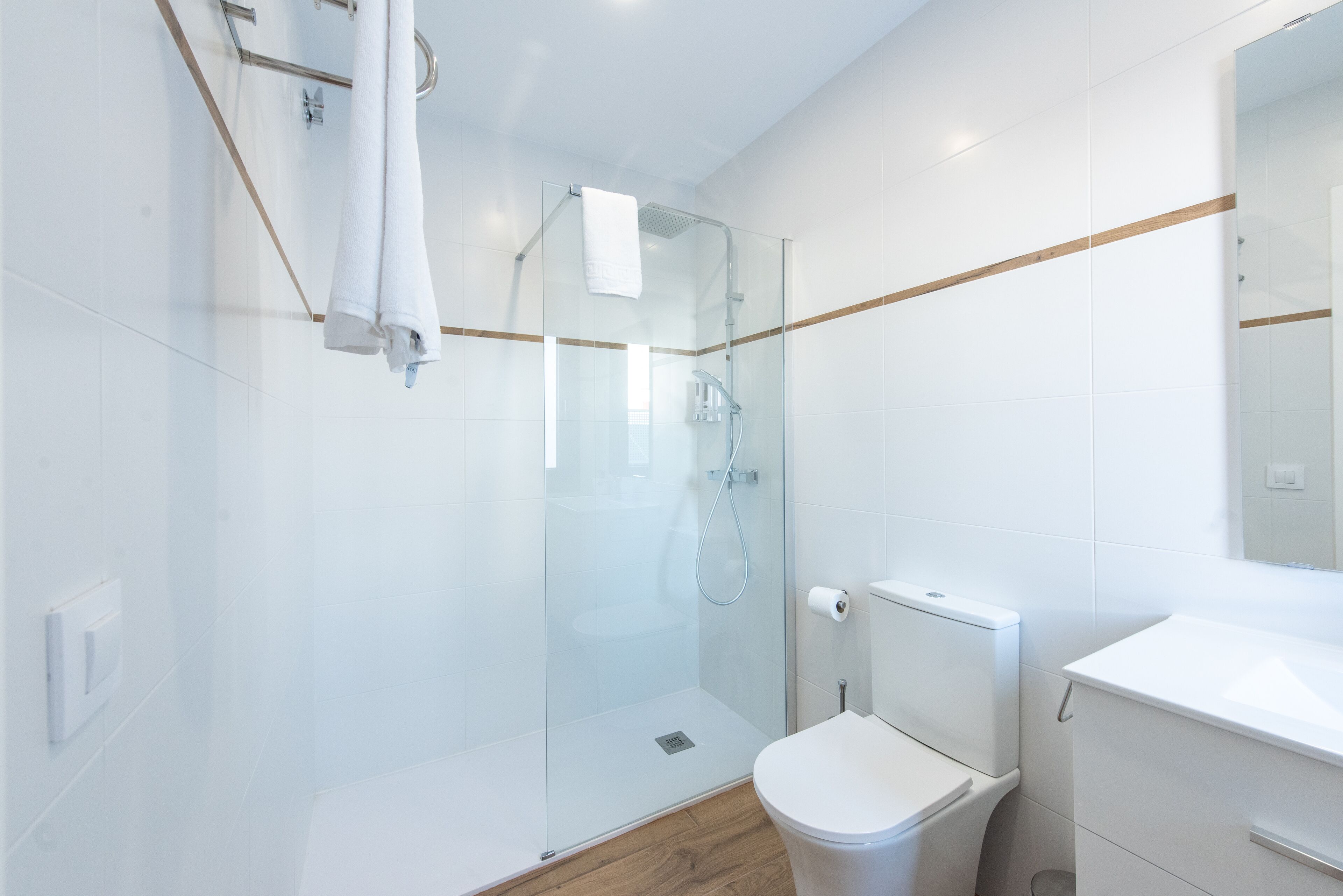 A modern bathroom with a glass-enclosed shower, a white toilet, and a wooden floor.