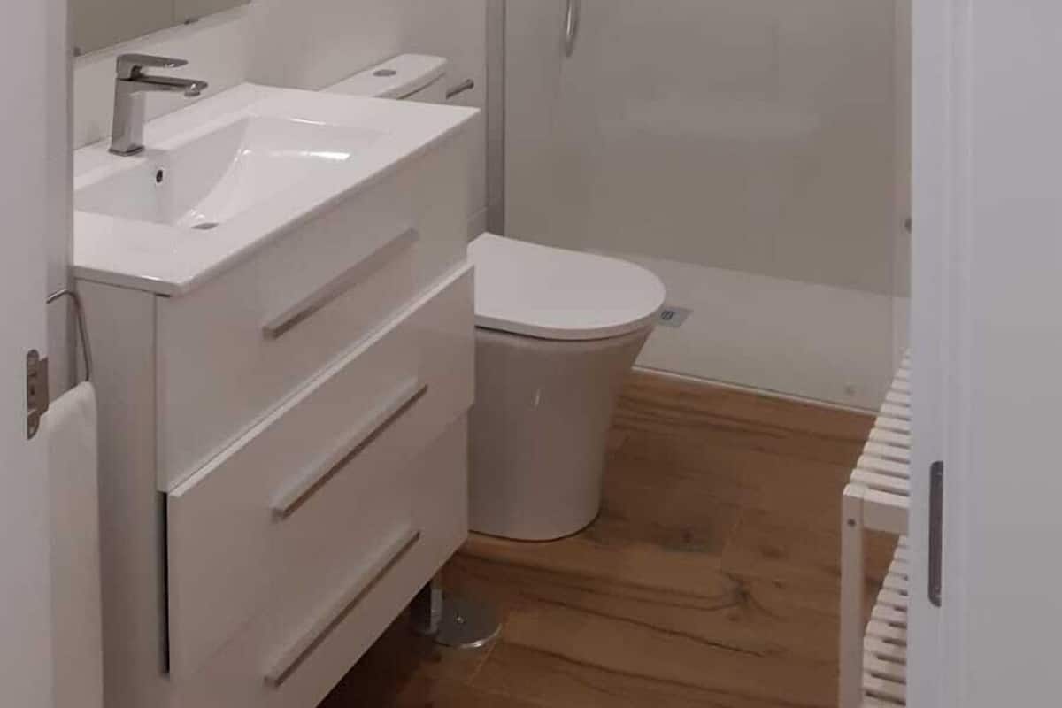 Een moderne badkamer met een douchecabine van glas, een wit wastafeltje en een toilet.