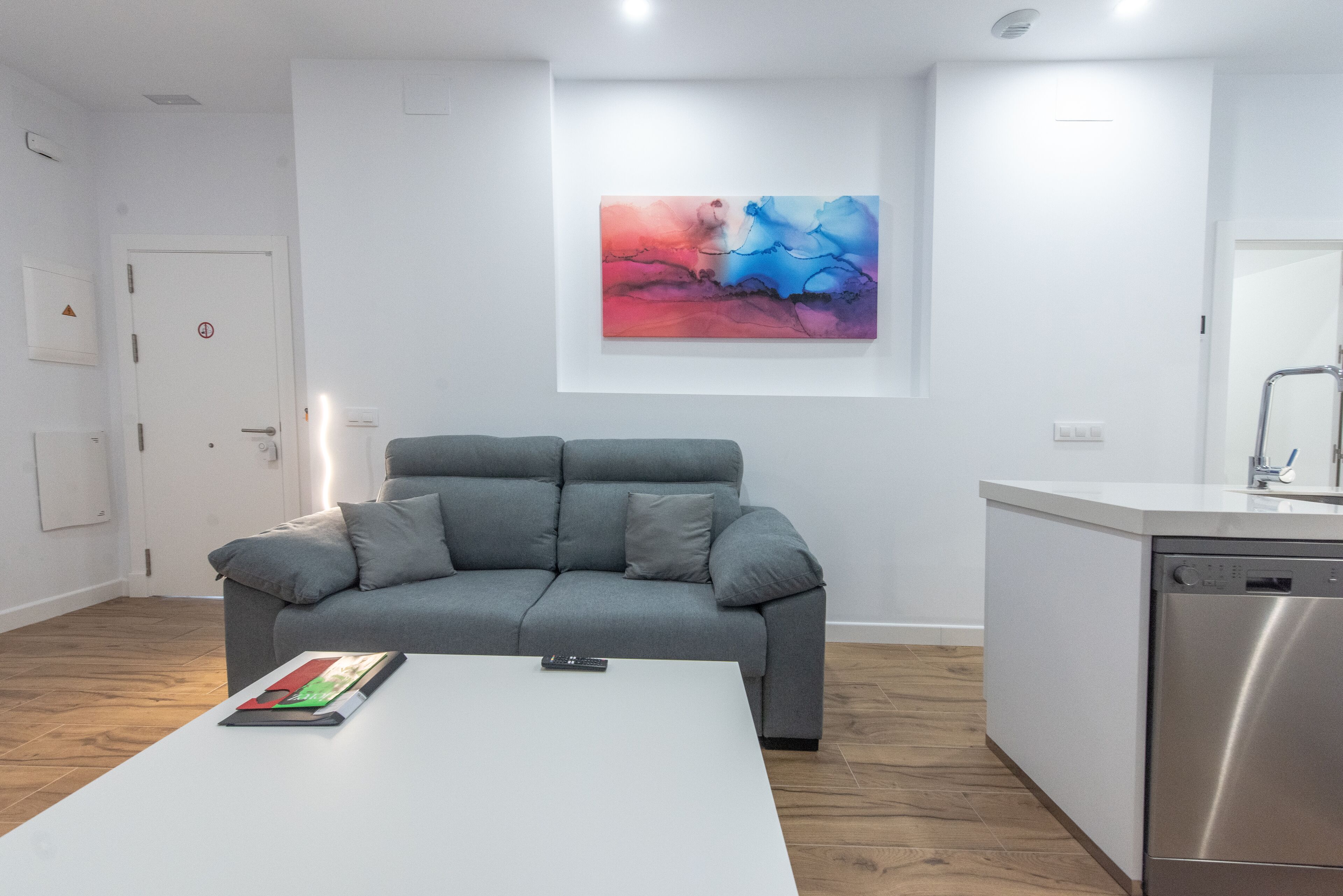 A modern living room with a grey sofa, a white coffee table, and a colorful abstract painting on the wall.