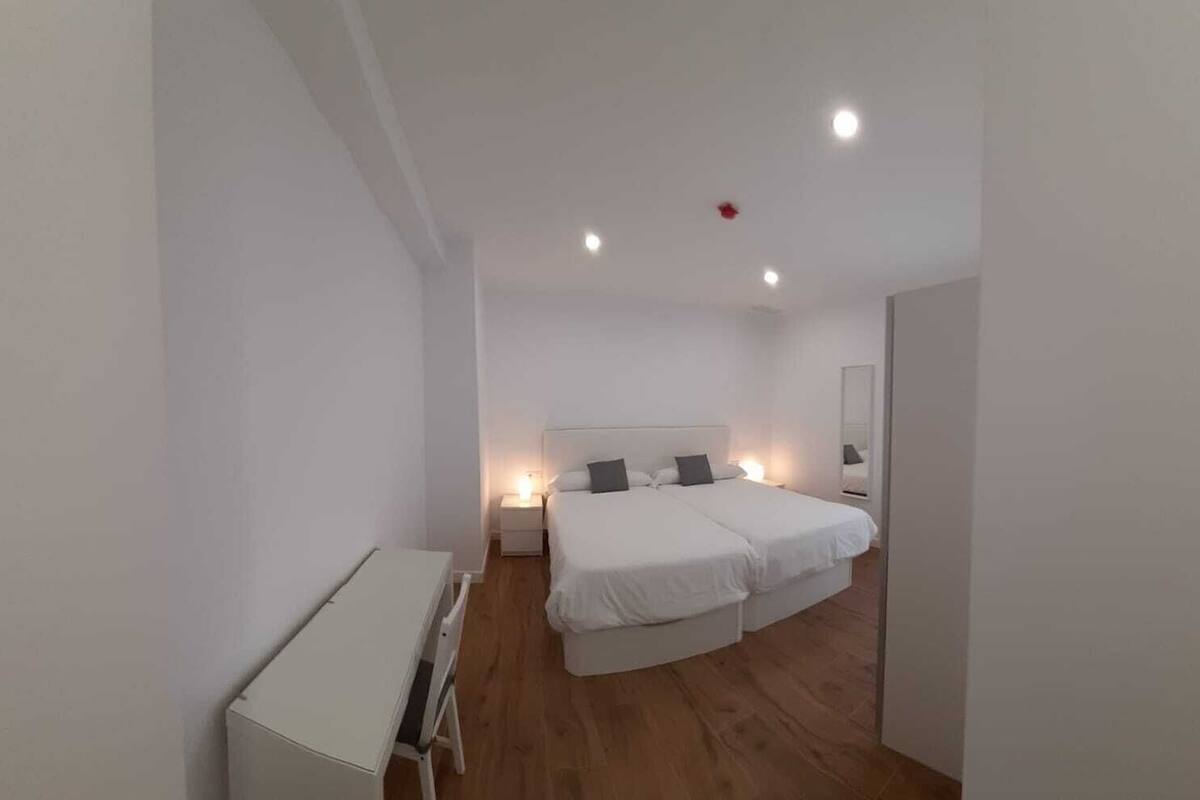 Een slaapkamer met een tweepersoonsbed, nachtkastjes, een bureau en een spiegel.