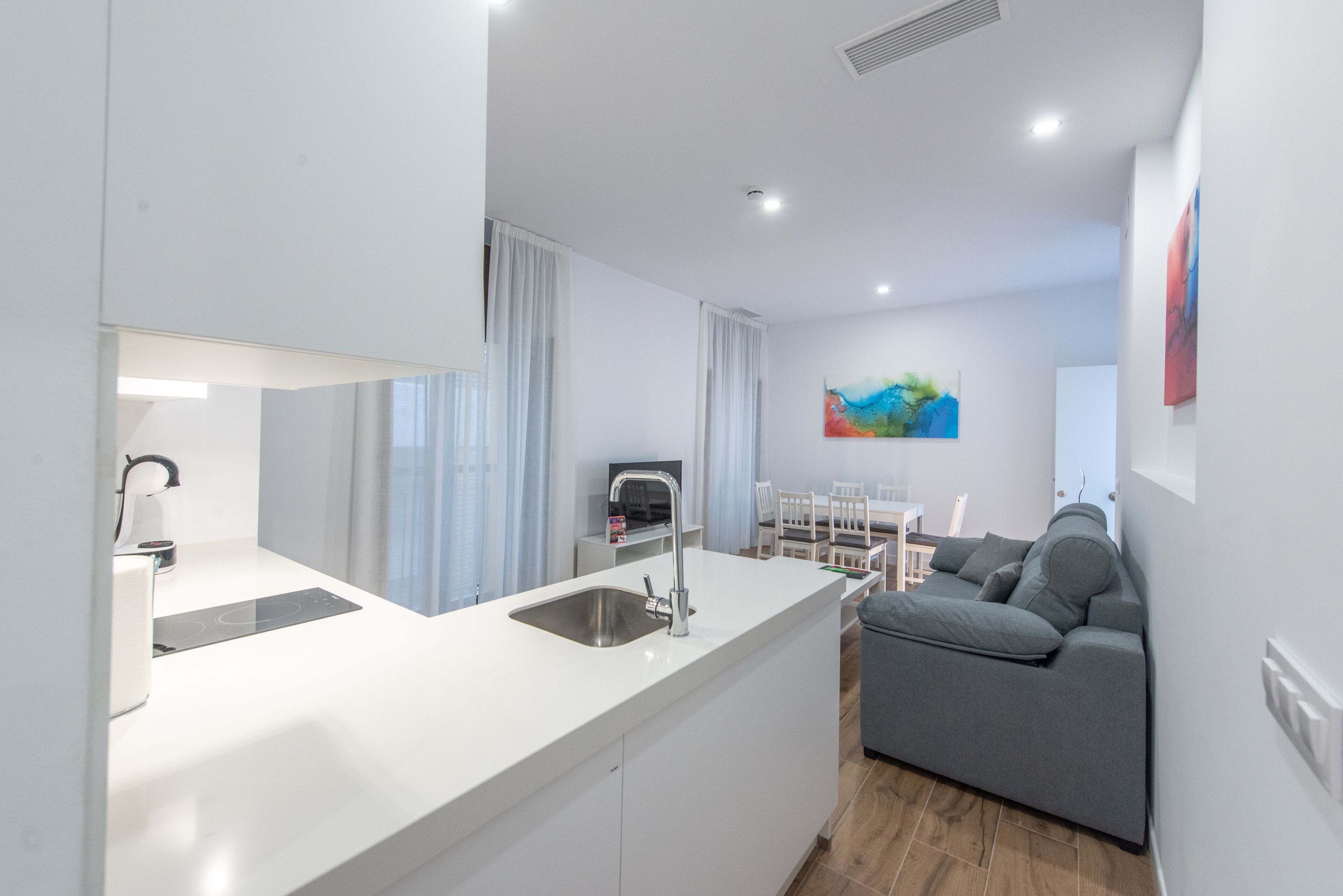 A modern kitchen with a built-in sink, a dining area with a table and chairs, and a gray sofa.