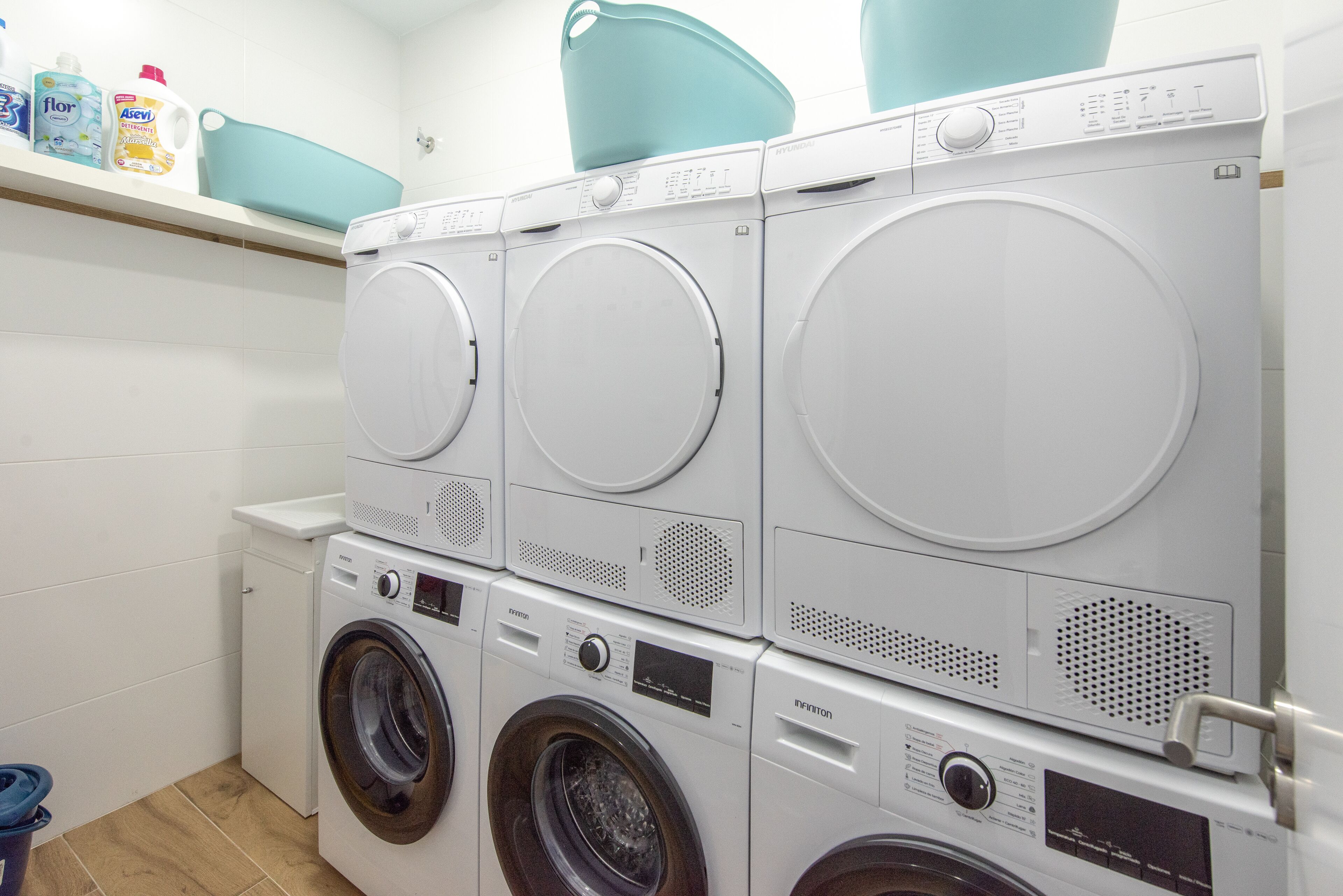 A laundry area with multiple washing machines and a shelf with cleaning products.