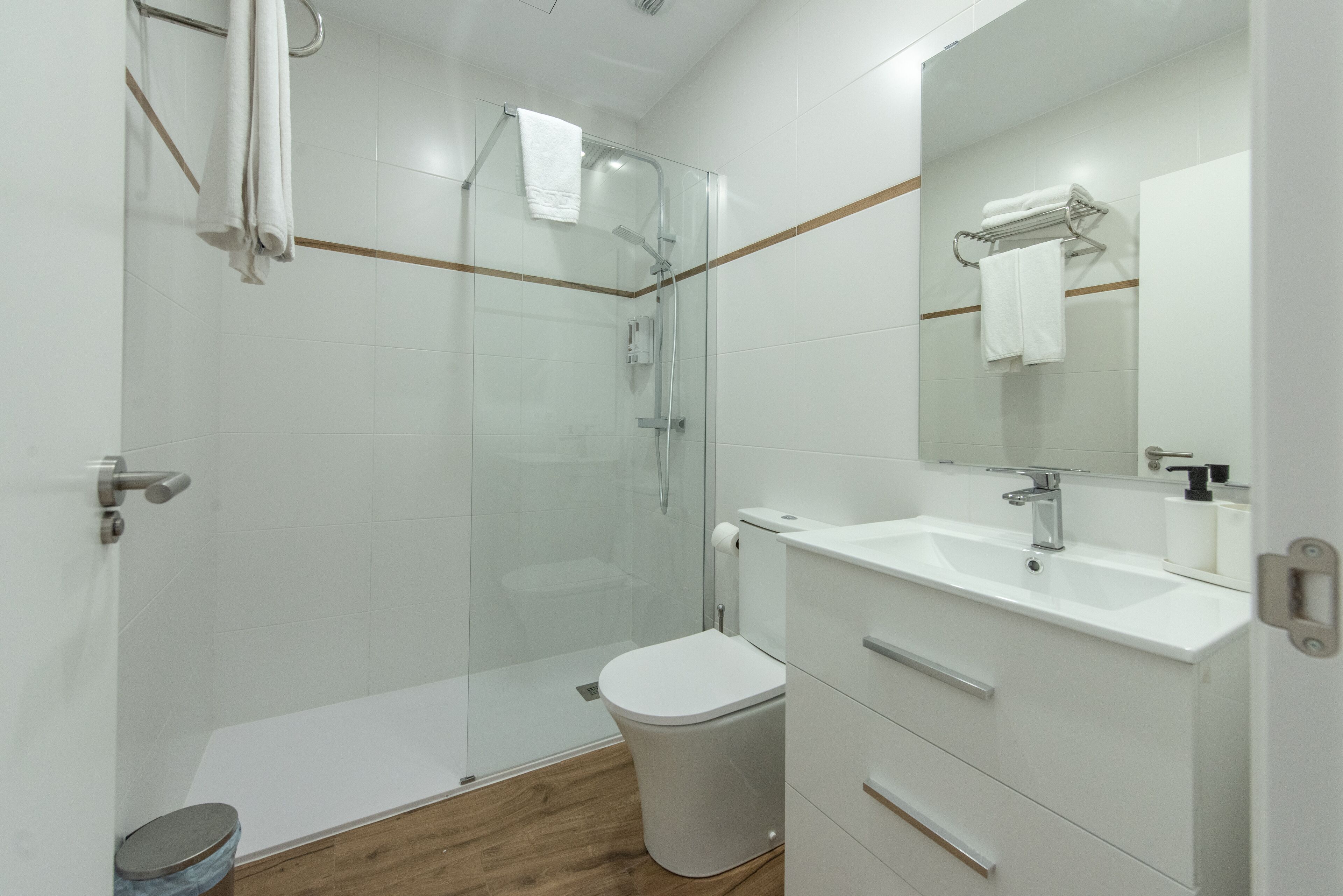 Une salle de bain moderne avec une douche à parois de verre, des toilettes blanches et un meuble-lavabo avec un miroir.
