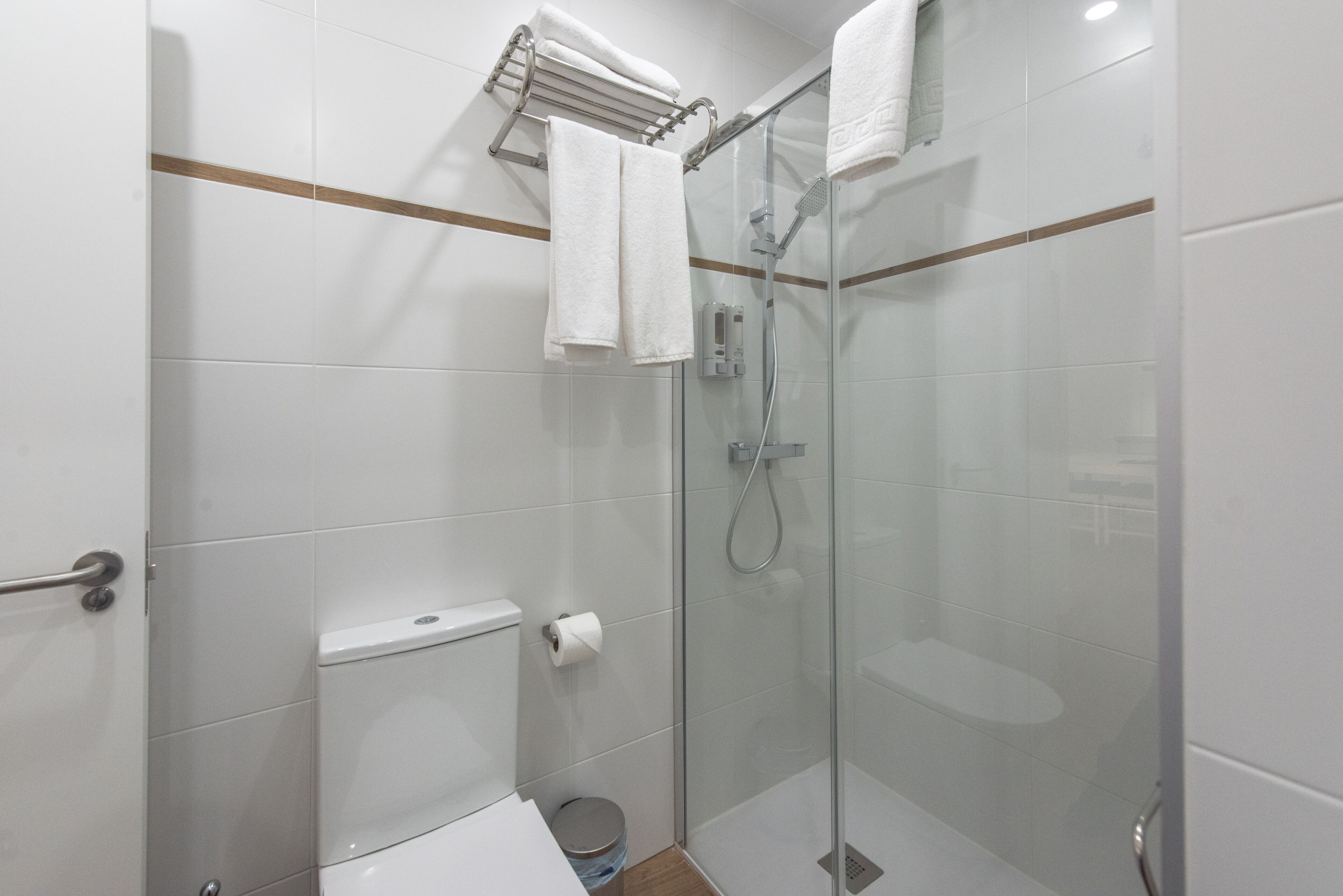 A modern bathroom with a glass-enclosed shower, a toilet, and a towel rack.