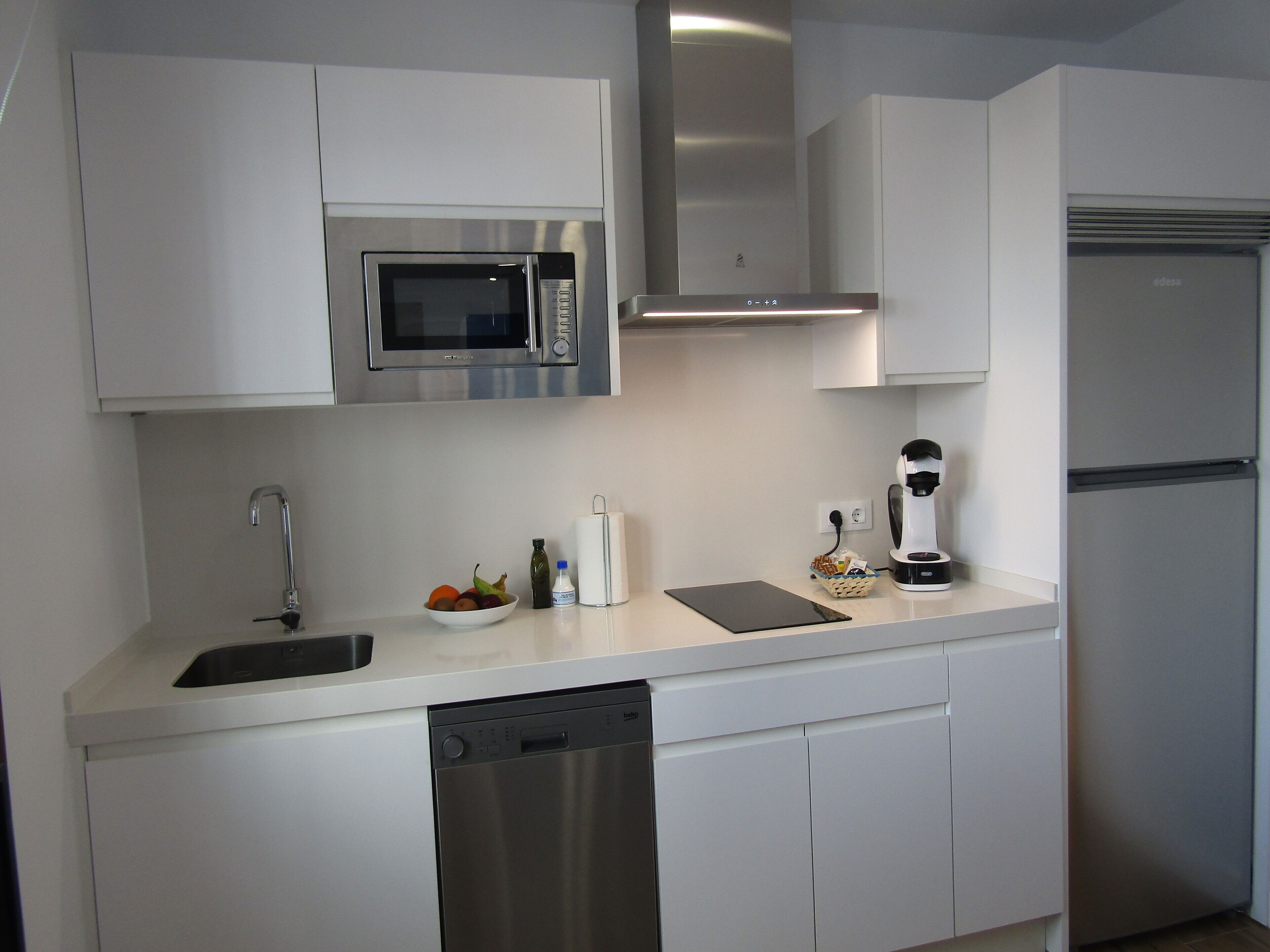 A modern kitchen with white cabinetry, a stainless steel microwave, a coffee maker, and a dishwasher.