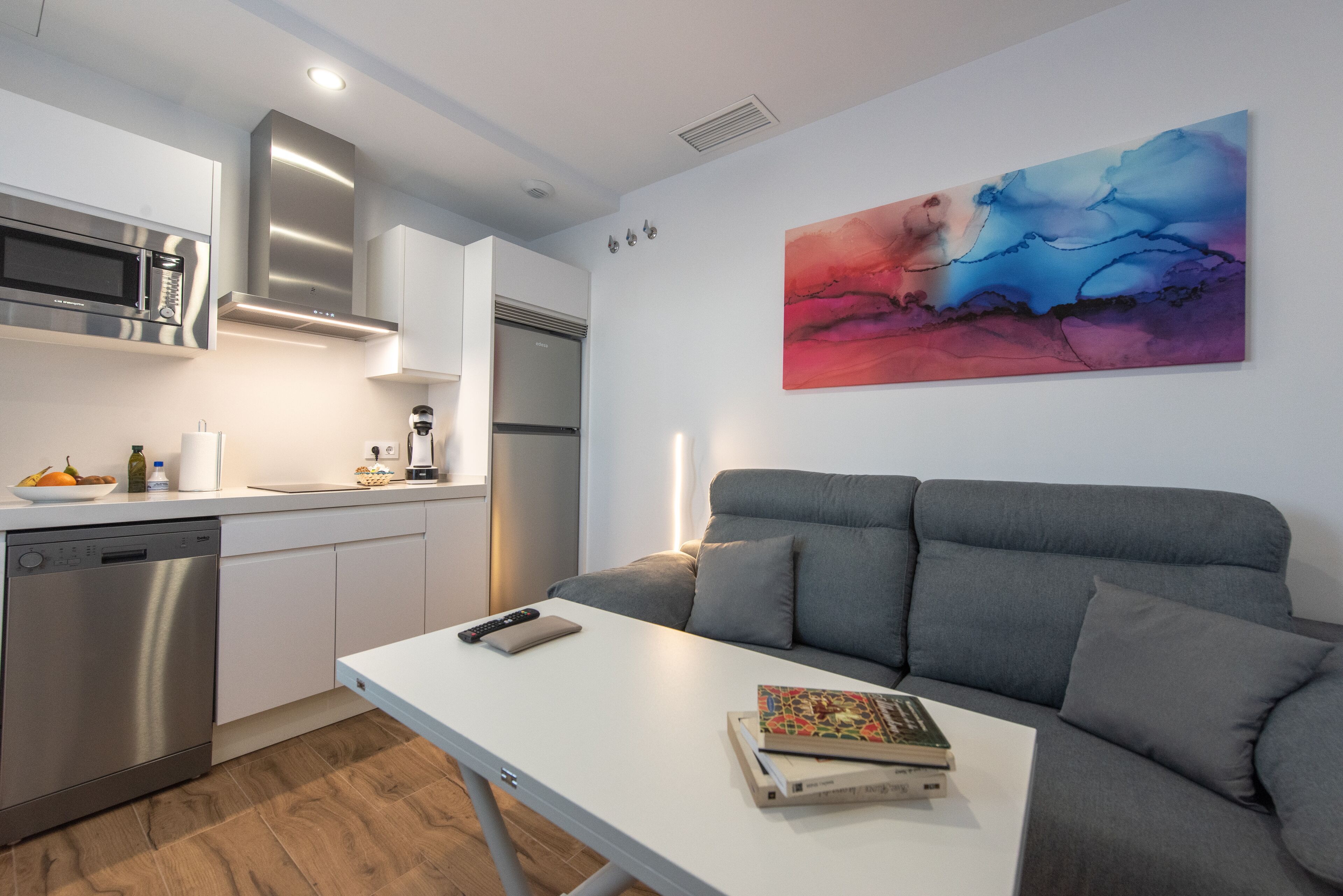 Una cocina moderna con electrodomésticos de acero inoxidable, un sofá gris y un cuadro en la pared.