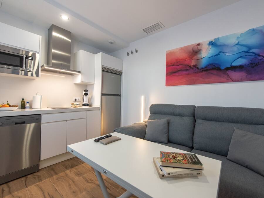 Una cocina moderna con electrodomésticos de acero inoxidable, un sofá gris y un cuadro en la pared.