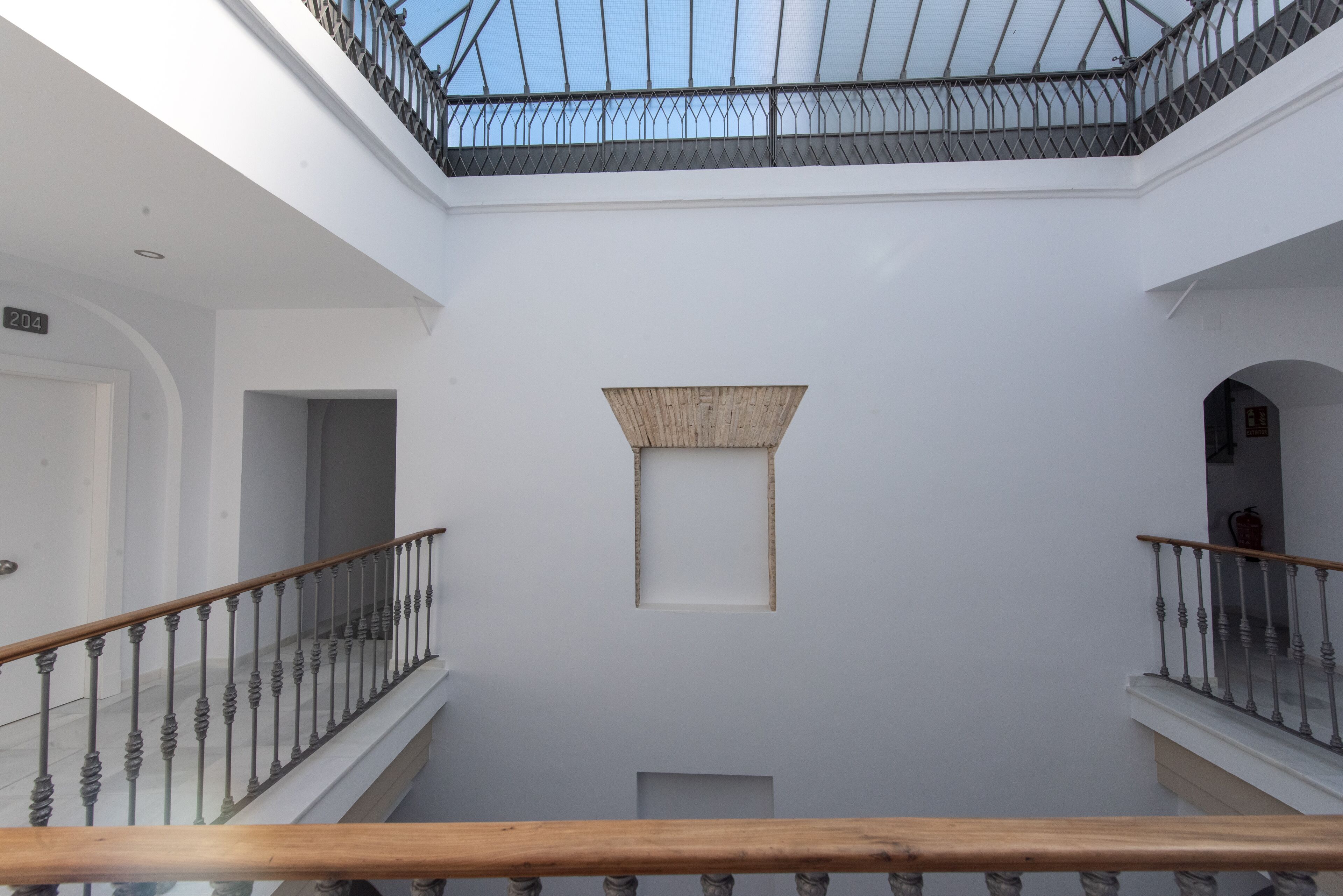 Un intérieur à plusieurs niveaux, doté d’un espace central ouvert, d’une rambarde en bois et d’une verrière.