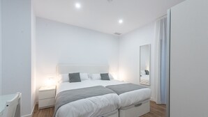 A modern bedroom with a large bed, bedside tables, a wardrobe, and a mirror. - Apartamentos Santa María 15 (Jerez de la Frontera)