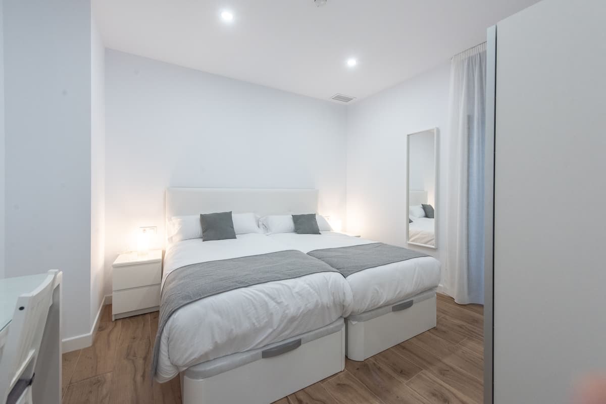 Een moderne slaapkamer met een groot bed, nachtkastjes, een kledingkast en een spiegel.