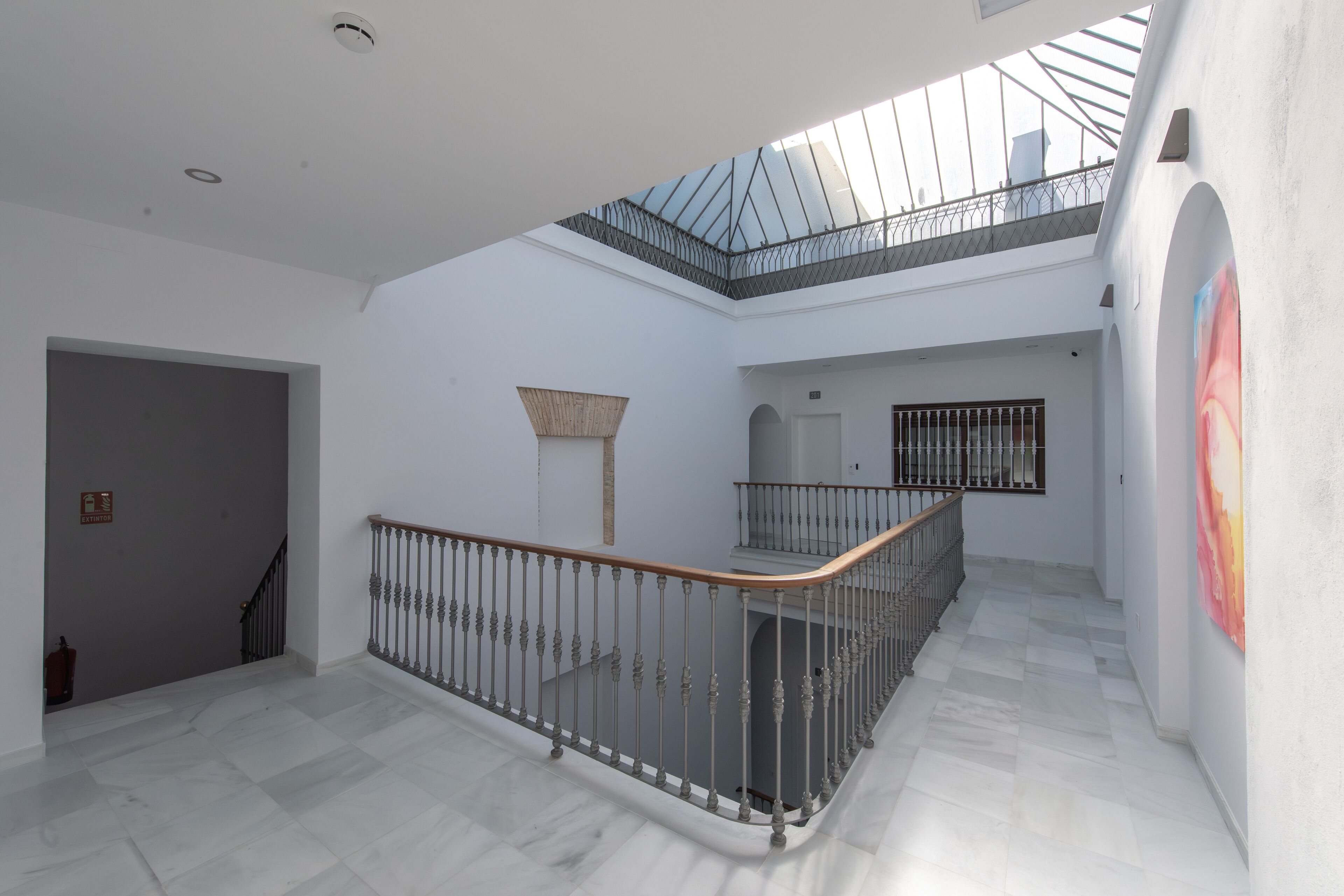 A spacious interior with a marble floor, a wooden railing, and a skylight.