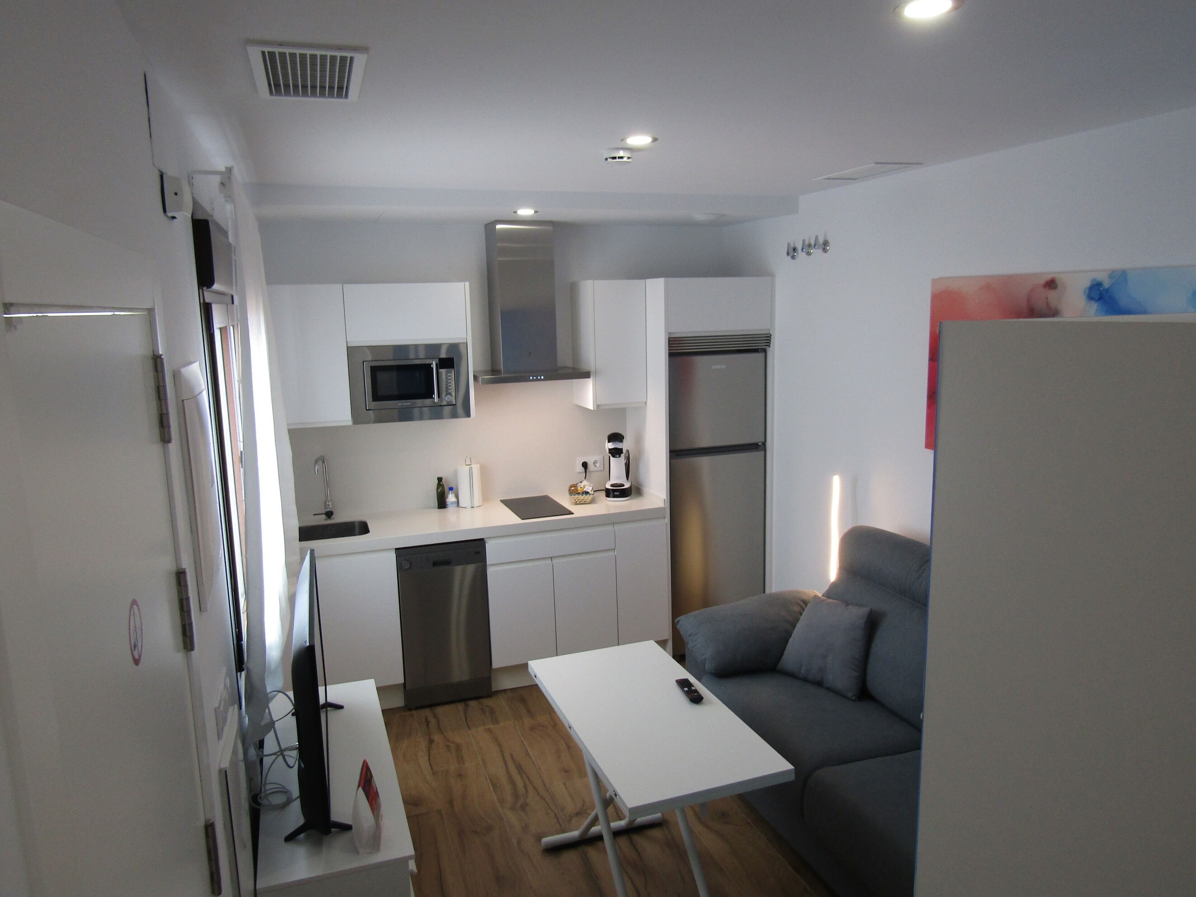 Una cocina compacta con electrodomésticos modernos, un comedor con mesa y un sofá, y un refrigerador a la vista.
