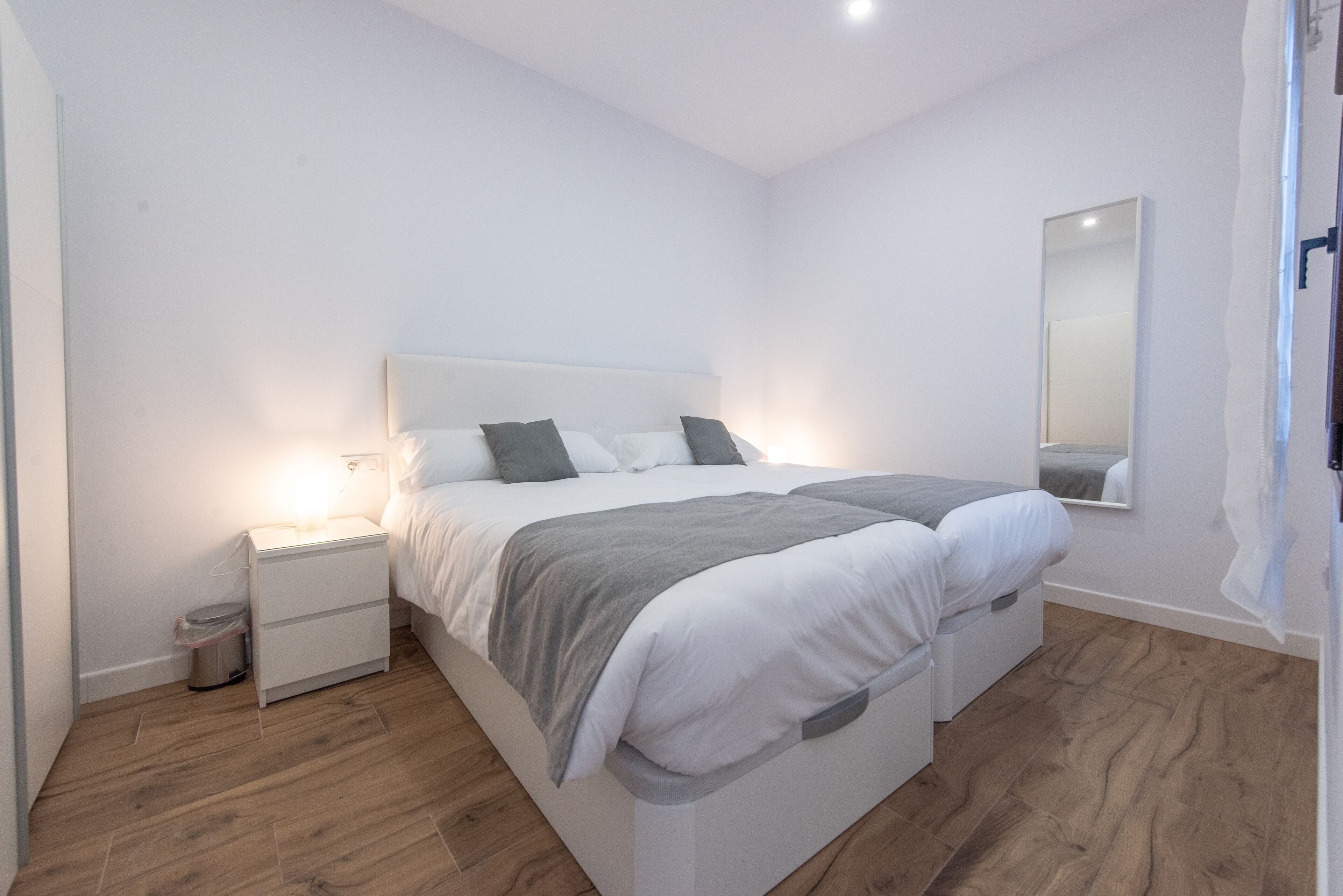 A modern bedroom with a large bed, bedside tables, and a mirror on the wall.
