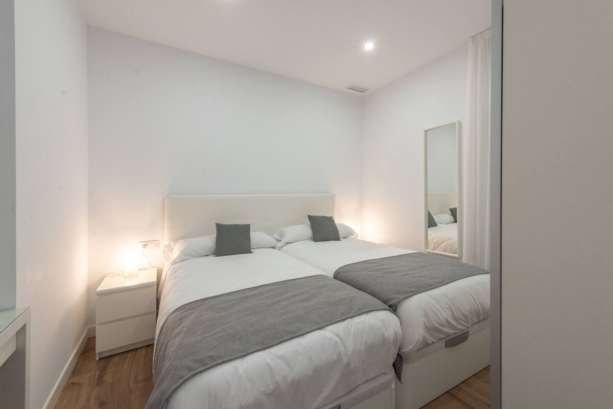 Een slaapkamer met twee bedden, een nachtkastje, een spiegel en een bedlampje.