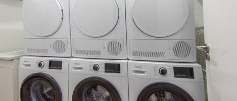 A stack of three front-loading washing machines and two top-loading washing machines in a laundry room.