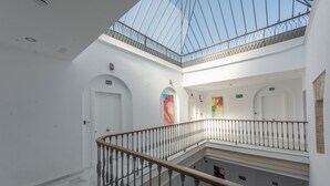A multi-level atrium with a glass ceiling, white walls, and a central staircase with a wooden handrail. - Apartamentos Santa María 15 (Jerez de la Frontera)