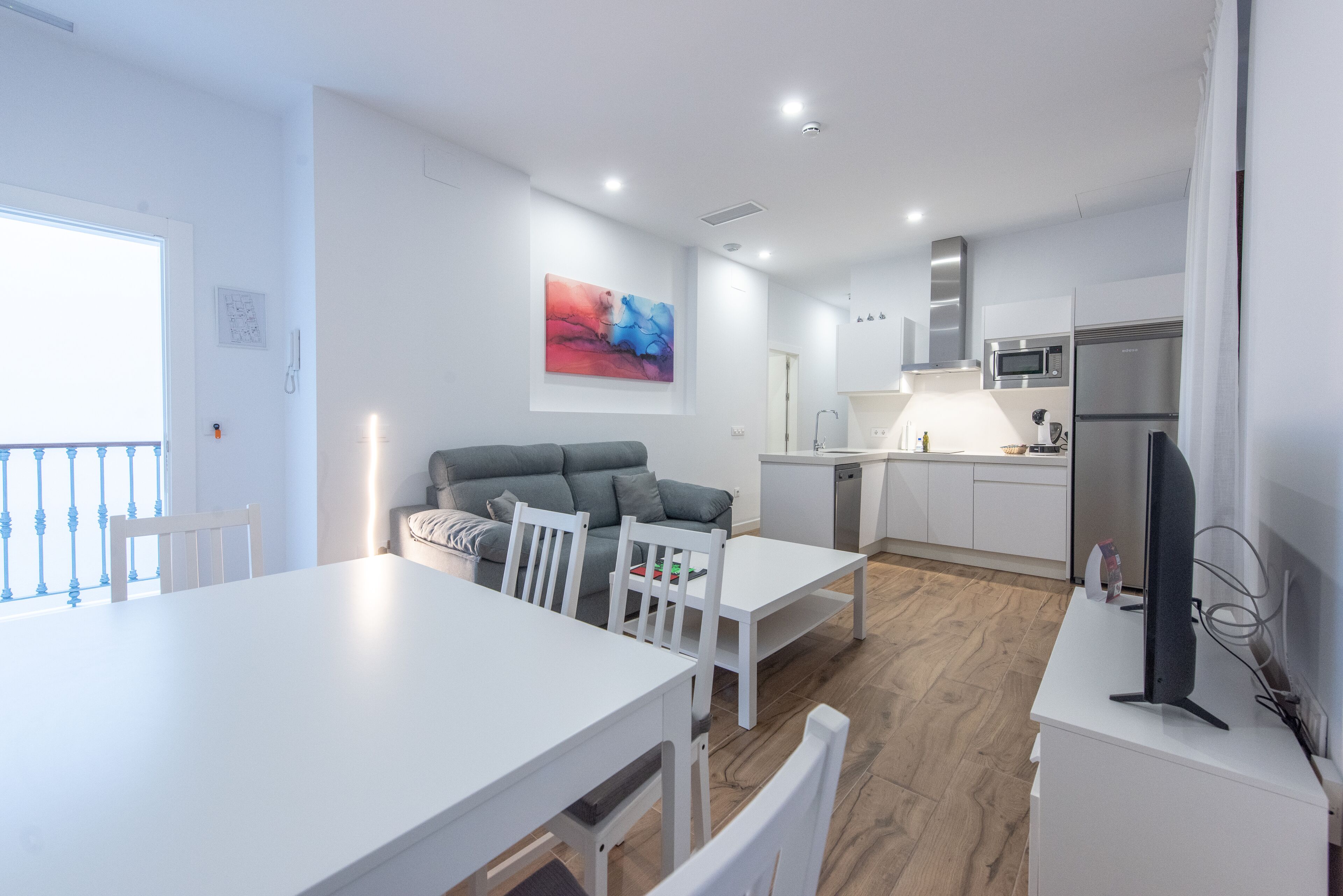 Een moderne keuken met witte kastjes, een grijze bank en een eettafel met stoelen.
