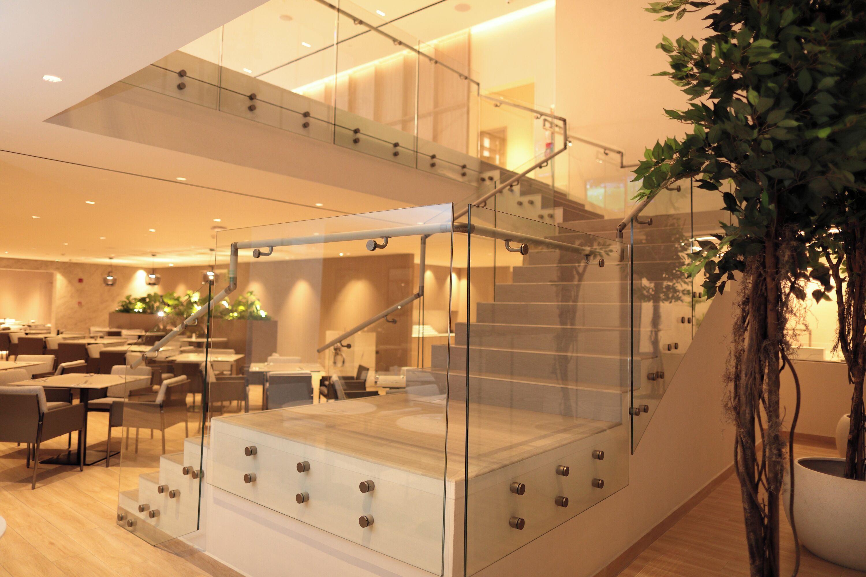 A modern hotel lobby with a glass staircase, seating area, and indoor plants.