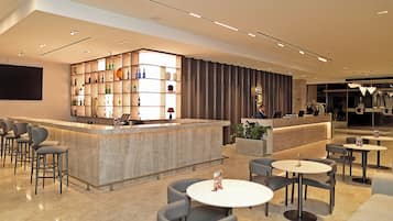 A modern bar area with a marble counter, seating with round tables, and a decorative bookshelf.