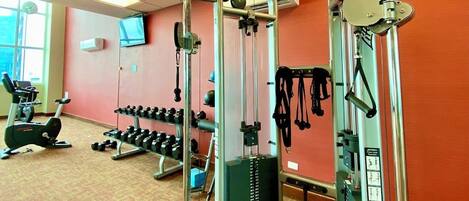 A gym with weightlifting equipment, dumbbells, and cardio machines.