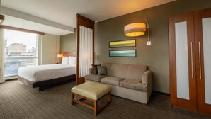 A hotel room with a bed, a sofa, an ottoman, a wall-mounted lamp, and a wardrobe. - Hotel Dann Carlton Panamá (Panama City)