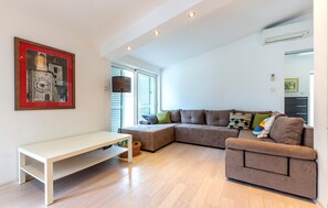 A modern living room with a sectional sofa, a small white table, and a large window with blinds.