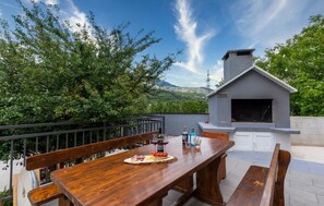 An outdoor patio with a wooden table set for dining, a built-in barbecue grill, and a scenic mountain backdrop.