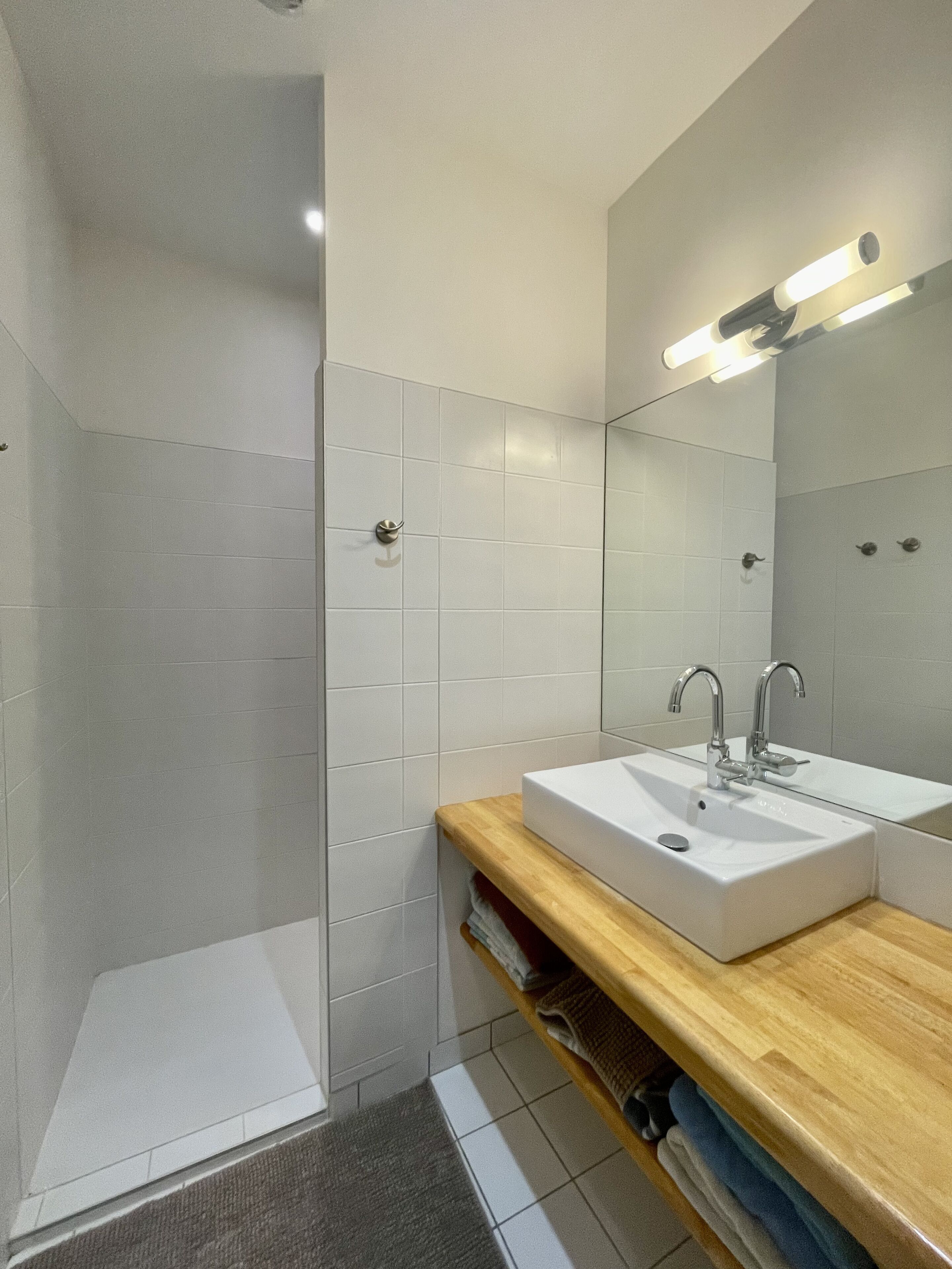 Une salle de bain moderne avec une douche à l’italienne, un lavabo avec un miroir et un meuble-lavabo en bois.
