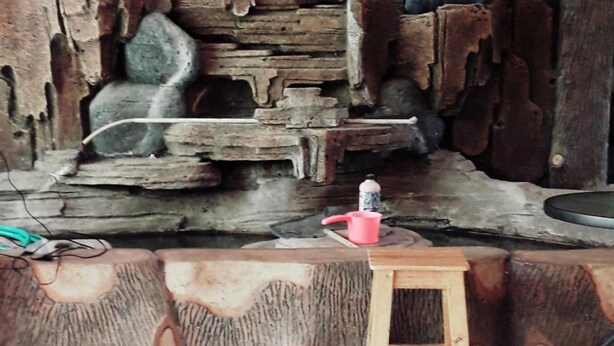 Un intérieur rustique avec un mur en pierre, un tabouret en bois et une tasse rouge posée sur une table.