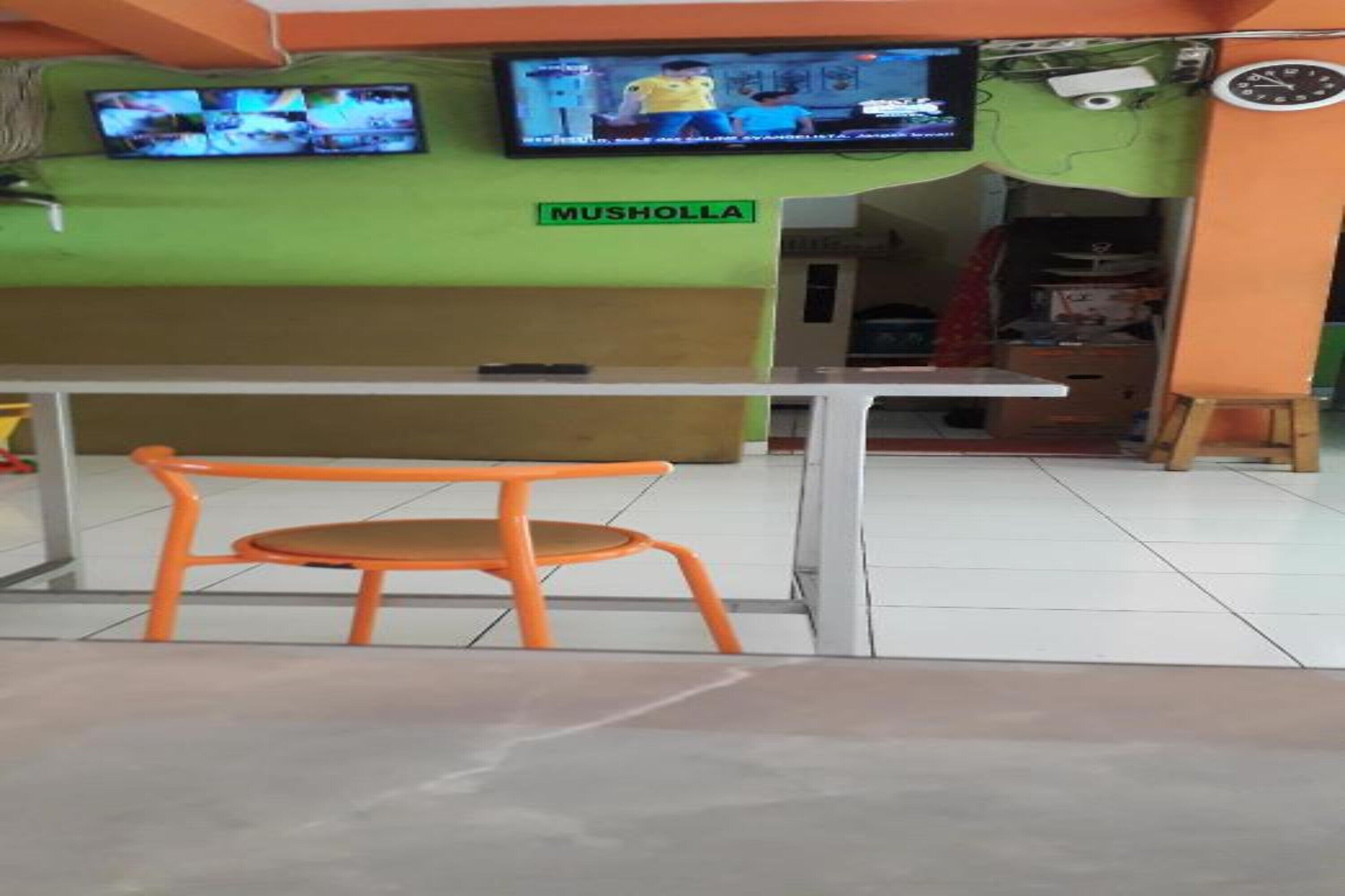 L’intérieur d’un restaurant avec un mur vert, un comptoir blanc et une chaise orange.