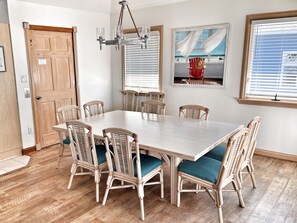 A dining room with a large wooden table surrounded by six wicker chairs with teal cushions.