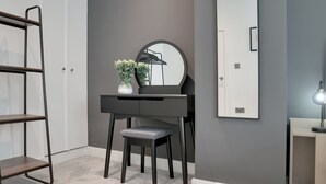 A room with a dark-colored vanity, a round mirror, a small stool, a shelf unit, and a potted plant. - Beam End Snainton - Modern 2-bedroom Stone Cottage. Pet Friendly. (Snainton)